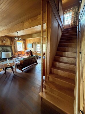 A wooden interior with a staircase, a fireplace, a dining area, and a view of the outdoors.