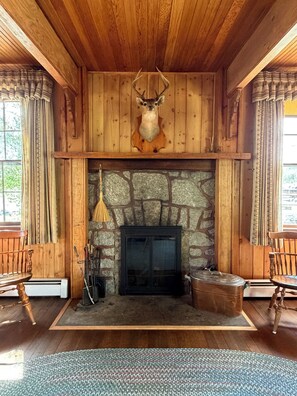 A rustic interior with a stone fireplace, wooden walls, and a deer head mounted above it.
