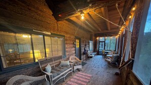 Ein gemütliches Blockhaus-Interieur mit Korbmöbeln, einem großen Fenster und Blick ins Freie.