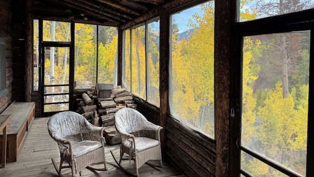 Eine Blockhütte mit großen Fenstern, Korbmöbeln und einer Holzterrasse.