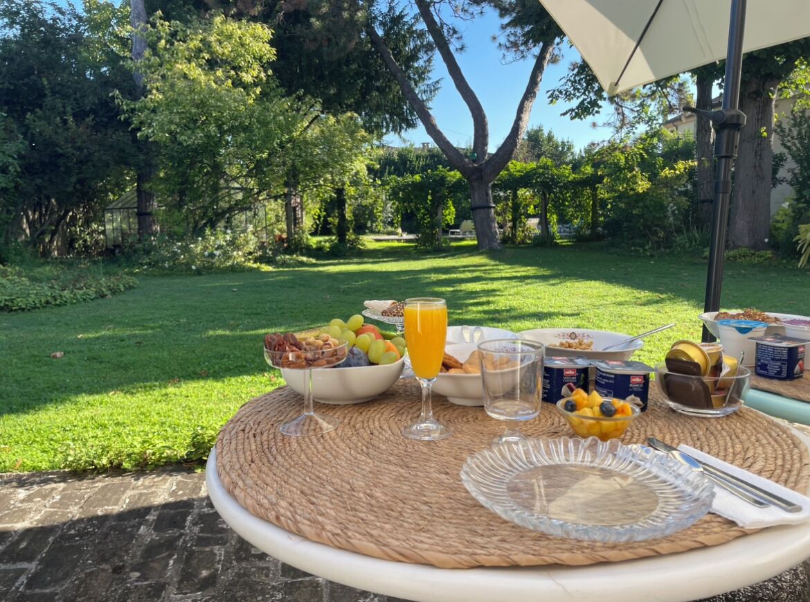 A breakfast setup on an outdoor table with a woven placemat, including bowls of fruit, a glass of orange juice, and various breakfast items.