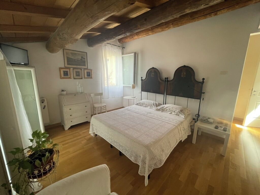 Un dormitorio con techo de madera, una cama con colcha blanca, una mesita de noche, un tocador y una planta en maceta.