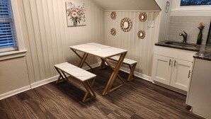 A kitchen with a white table and bench, wooden flooring, and decorative wall art. - Private 2BR Apartment w/ Private Entrance – Entire Upstairs Unit (Portsmouth)