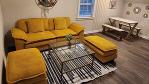 A cozy living room with a yellow sofa, a glass coffee table, and a matching ottoman. There's a wooden bench and a small table with a white tablecloth. - Private 2BR Apartment w/ Private Entrance – Entire Upstairs Unit (Portsmouth)