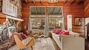 Una sala de estar acogedora con chimenea de piedra, vigas de madera y un ventanal con vistas a una terraza.