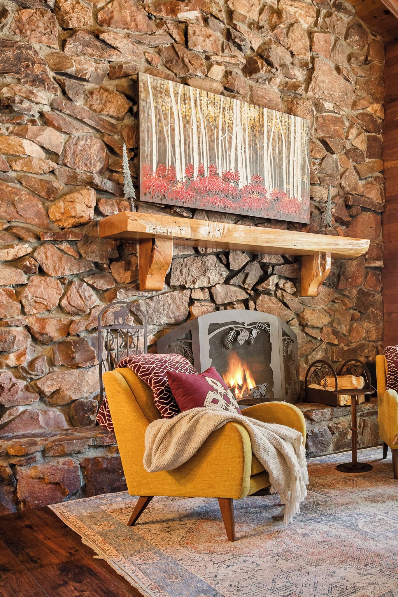 Una sala de estar acogedora con una pared de piedra, una chimenea, un sillón amarillo y un cuadro decorativo sobre la repisa.