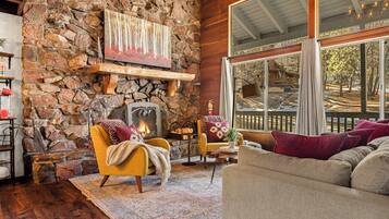 Una sala de estar acogedora con chimenea de piedra, vigas de madera y grandes ventanales que dan a una terraza.