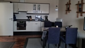 A compact kitchen with white cabinets, a coffee maker, and a dining area with two chairs. - Cozy apartment Strandallee in Burg/Fehmarn. (Burg/Fehmarn)