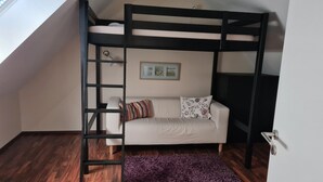 A bunk bed with a ladder, a sofa with patterned cushions, a purple rug, and a framed picture on the wall. - Cozy apartment Strandallee in Burg/Fehmarn. (Burg/Fehmarn)