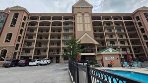 Ein Mehrstöckiges Hotel mit einem zentralen Atrium, Balkonen auf jeder Etage und einem Poolbereich mit Liegestühlen.