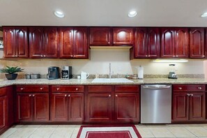 A kitchen with dark wooden cabinets, a stainless steel dishwasher, and a granite countertop. - Creekside Condo with Pool, Walk Downtown (Gatlinburg)