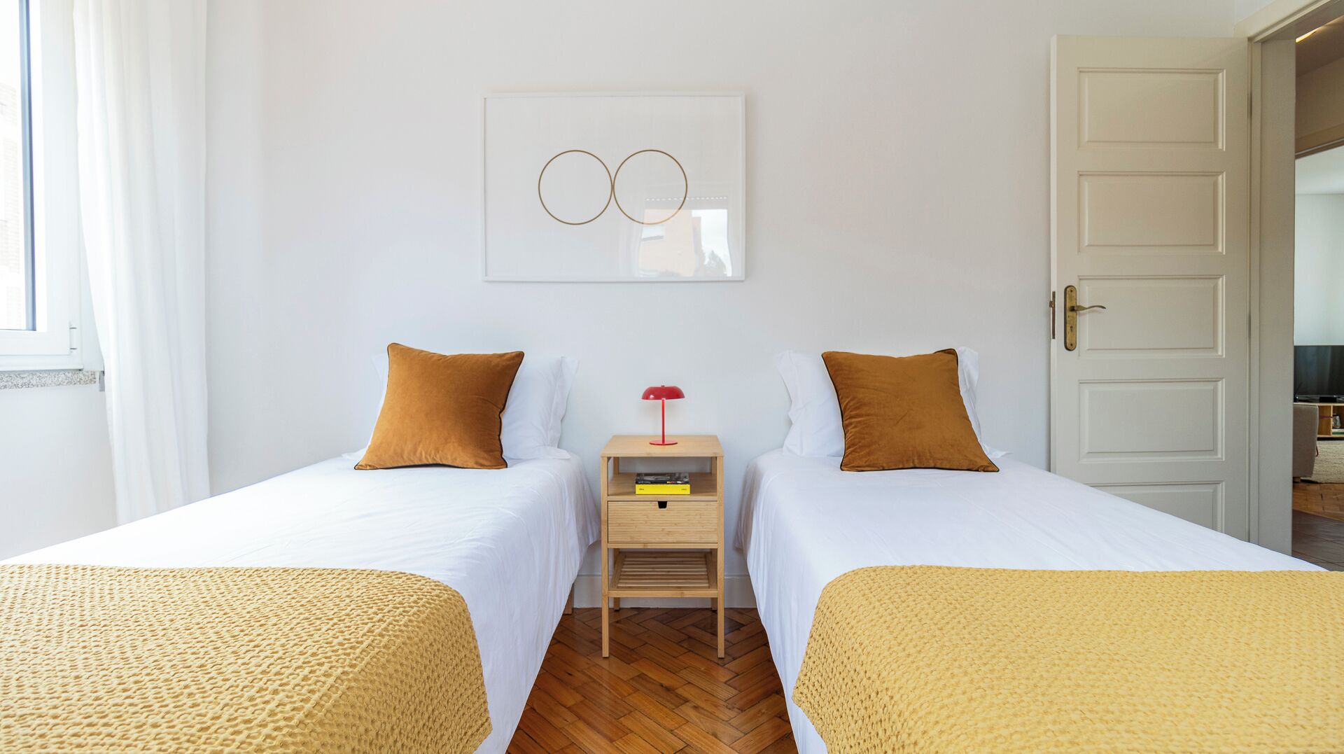 A double room with two beds, a nightstand with a lamp, and a framed artwork on the wall.