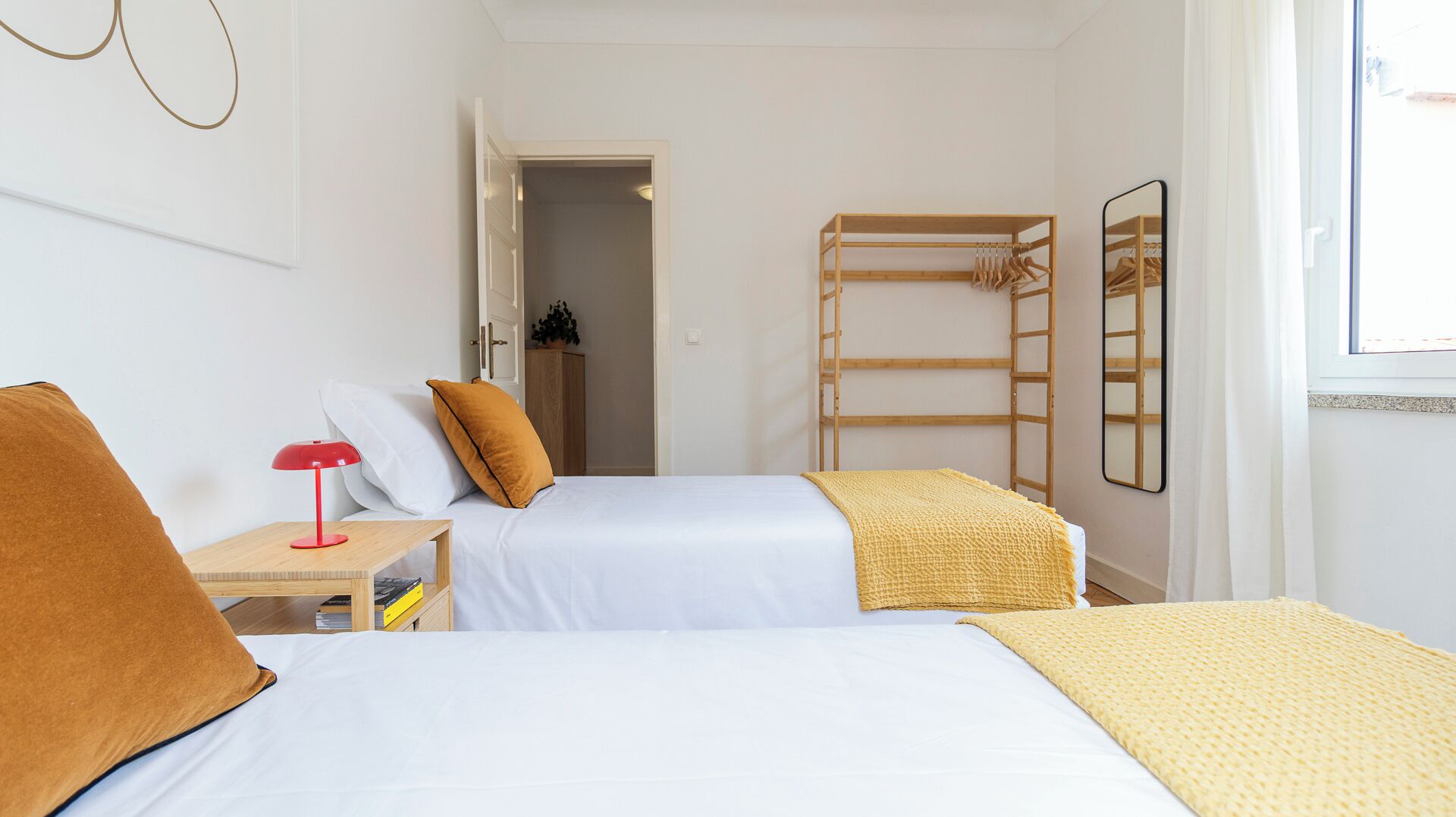 Une chambre avec deux lits, une lampe rouge, une échelle en bois et un miroir au mur.