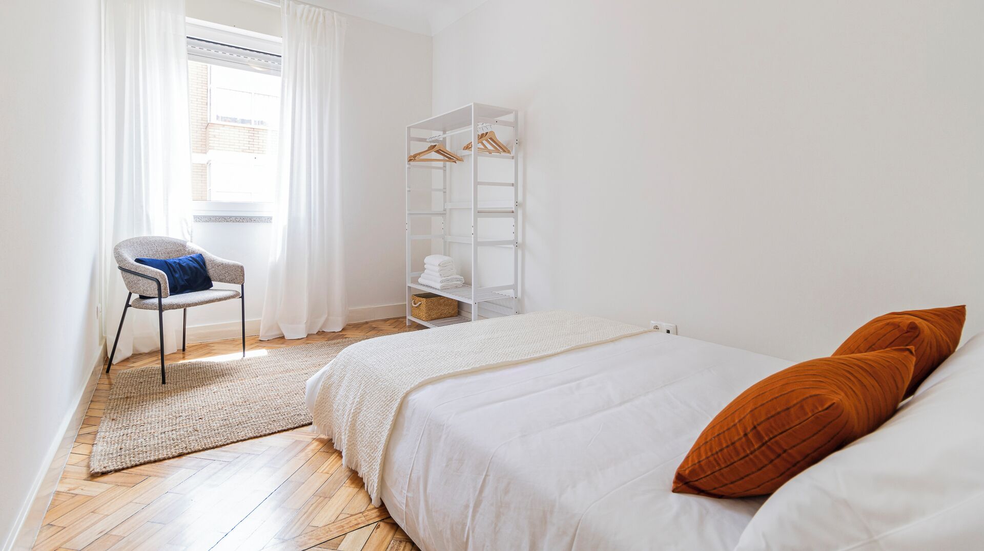 A bedroom with a bed, a chair, a wardrobe, and a window with curtains.