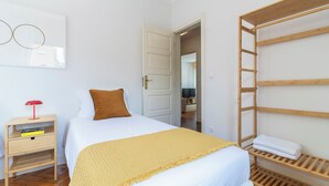 A bedroom with a bed, a bedside table with a lamp, a wooden shelf with towels, and a door leading to another room. - Fully equipped apartment in Barroselas, Viana do Castelo (Barroselas)