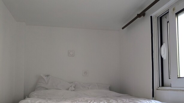 A simple, unadorned bedroom with a single bed, a window, and basic furnishings.