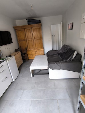 Ein kompakter Wohnraum mit einer Couch, einem kleinen Tisch, einem Holzschrank, einem Fernseher und einer Tür.