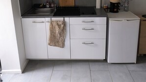 A compact kitchen with white cabinets, a built-in stove, and a small refrigerator.