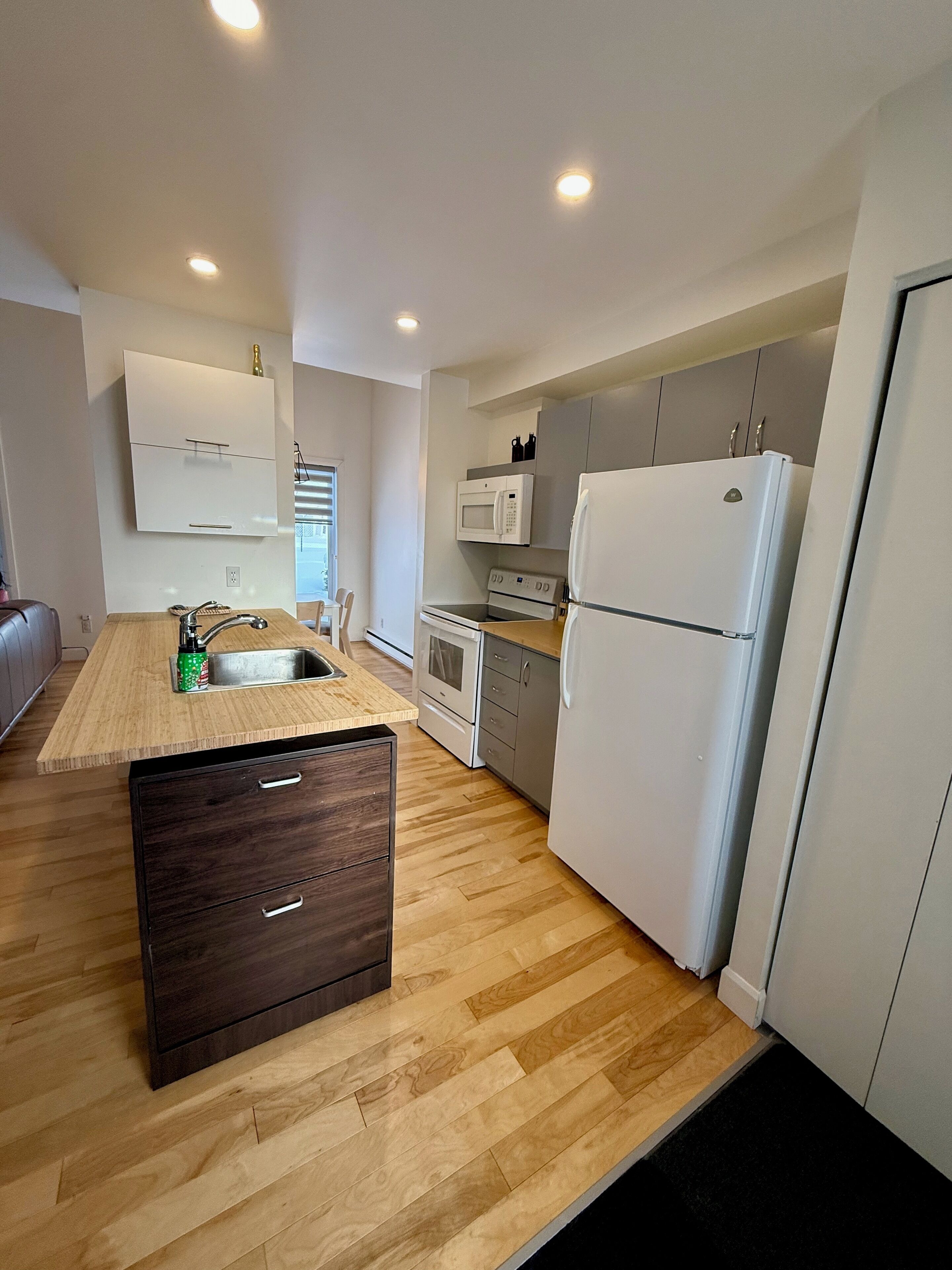 A modern kitchen with wooden flooring, a built-in sink, a microwave, a stove, and a refrigerator.
