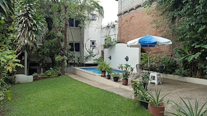 Un petit jardin à l’arrière de la maison, avec une piscine, entouré de plantes en pot et d’un mur de briques.