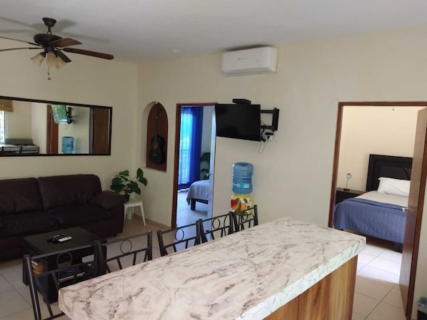 Un espace de vie compact doté d’un comptoir en marbre, d’un ventilateur de plafond, d’un téléviseur fixé au mur, d’une guitare et d’un lit recouvert d’une courtepointe bleue.