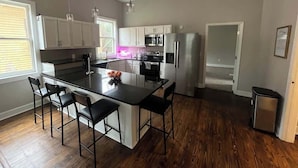 Una cocina moderna con una isla central, taburetes de bar, electrodomésticos de acero inoxidable y suelo de madera.