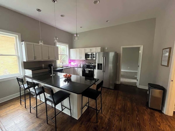 A modern kitchen with a central island, bar stools, stainless steel appliances, and wooden flooring.