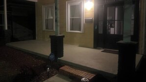 Una casa con un porche cubierto, una puerta de garaje y un bote de basura.