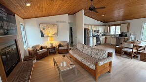 A spacious living area with a wooden ceiling, a sofa, chairs, a coffee table, a fireplace, and a kitchen in the background. - Waterfront, Dock, Deck, Walk to the Beach, bring your kayaks/boat! (South Bethany)