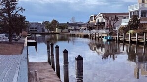 A wooden dock extending into calm water with a reflection of nearby houses and a cloudy sky. - Waterfront, Dock, Deck, Walk to the Beach, bring your kayaks/boat! (South Bethany)