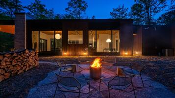 A modern outdoor seating area with a fire pit, surrounded by chairs and a stone wall.