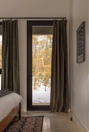 Un dormitorio con una cama, una puerta que da a un área exterior nevada y una alfombra estampada.