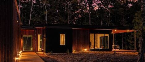 A modern cabin with a wooden exterior, a covered patio, and a pathway leading to the entrance.