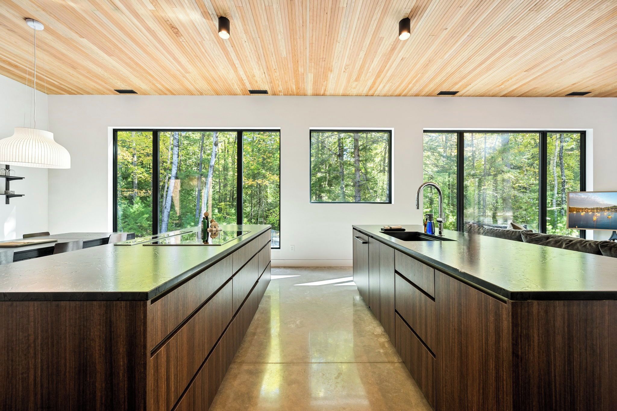 Een moderne keuken met een centraal eiland, grote ramen en een houten plafond.