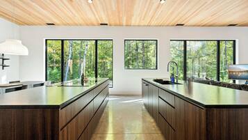 Een moderne keuken met een centraal eiland, grote ramen en een houten plafond.