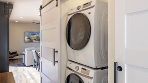 Una sala de bugaderia amb dues rentadores apilades, un terra de fusta i una porta corredissa.
