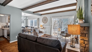 Un vaste espace de vie comprenant un canapé en cuir foncé, une table à manger avec des chaises, un lustre et une cheminée en pierre.
