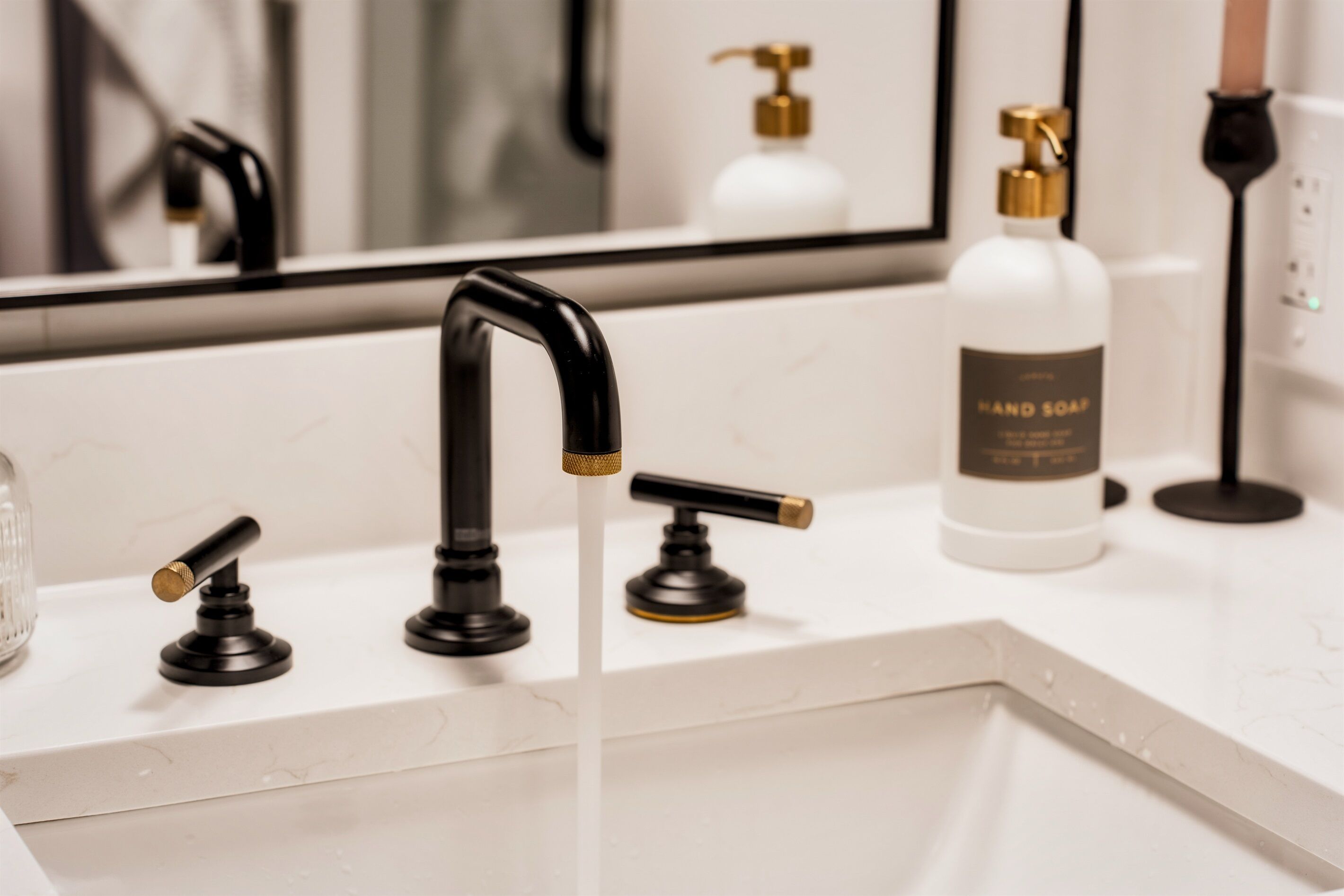 A bathroom with a white sink, black faucet, and a bottle of hand soap.