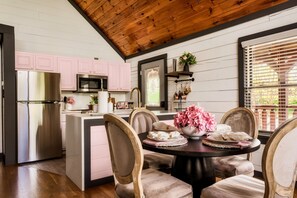 Une cuisine avec des meubles de couleur rose, un réfrigérateur en acier inoxydable et un coin repas comprenant une table ronde et des chaises.