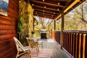 Une terrasse en bois avec un muret en pierre, un barbecue, des chaises en osier et une table.