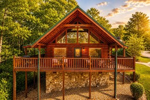 Une cabane en rondins dotée d’un balcon, avec des fondations en pierre, et entourée d’arbres.