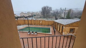 Vista de una piscina con solárium de baldosas y algunas sillas, rodeada por un muro bajo y un edificio con tejado de cerámica.