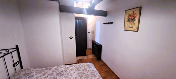 A narrow hallway with a bed at the end, a door leading to another room, and a radiator on the wall.
