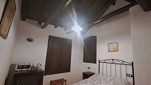 Un dormitorio con cama, cómoda, mesita de noche, estante en la pared y luz de techo.