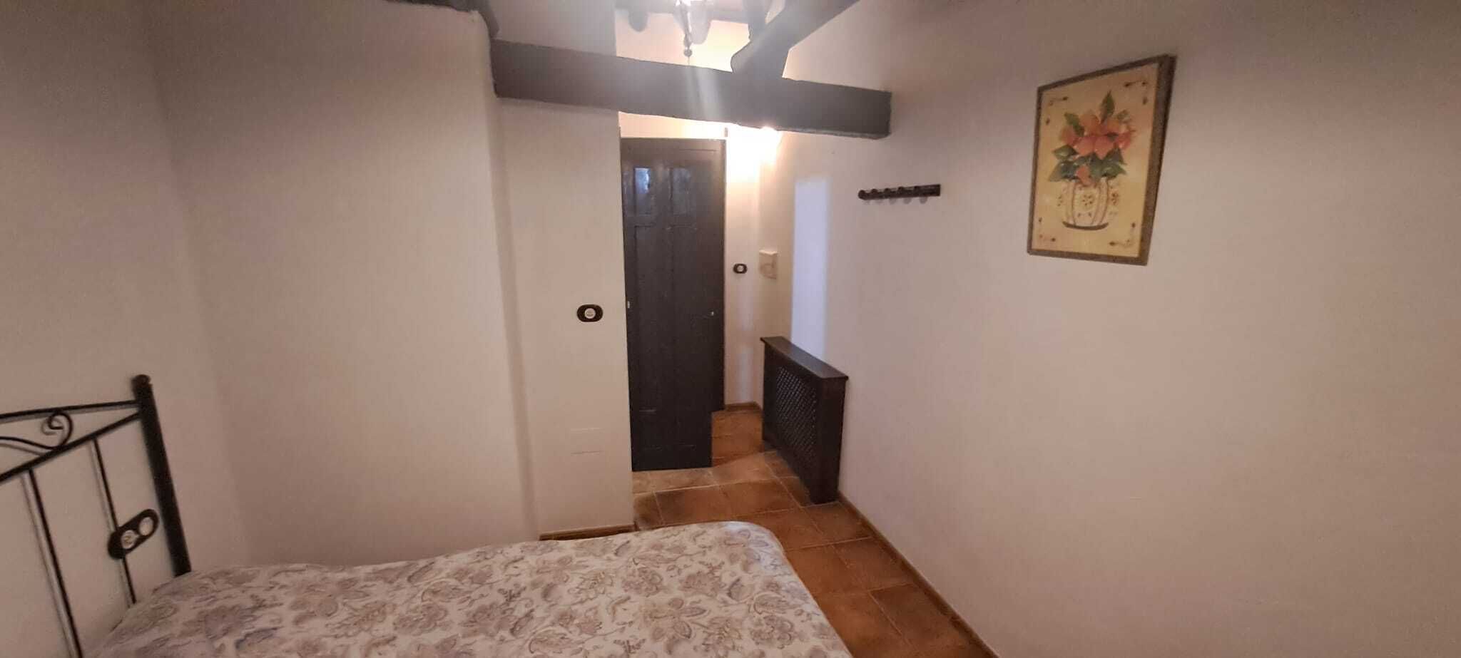 A narrow hallway with a bed at the end, a door, and a radiator on the wall.