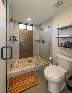 Uma casa de banho moderna com cabine de duche em vidro, sanita e prateleira embutida com produtos de higiene pessoal.
