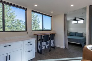 Ein gemütliches Schlafzimmer mit Bett, kleinem Schreibtisch mit zwei Stühlen und einem Fenster mit Blick auf Bäume.