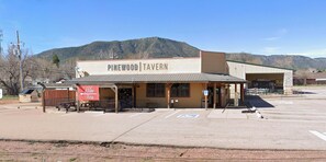 Uma Taberna Pinewood com área de estar coberta ao ar livre, um estacionamento e um cenário montanhoso.