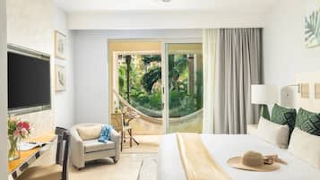 Habitación de hotel con una cama, un escritorio con silla, televisión y vistas a un jardín por una puerta de cristal.
