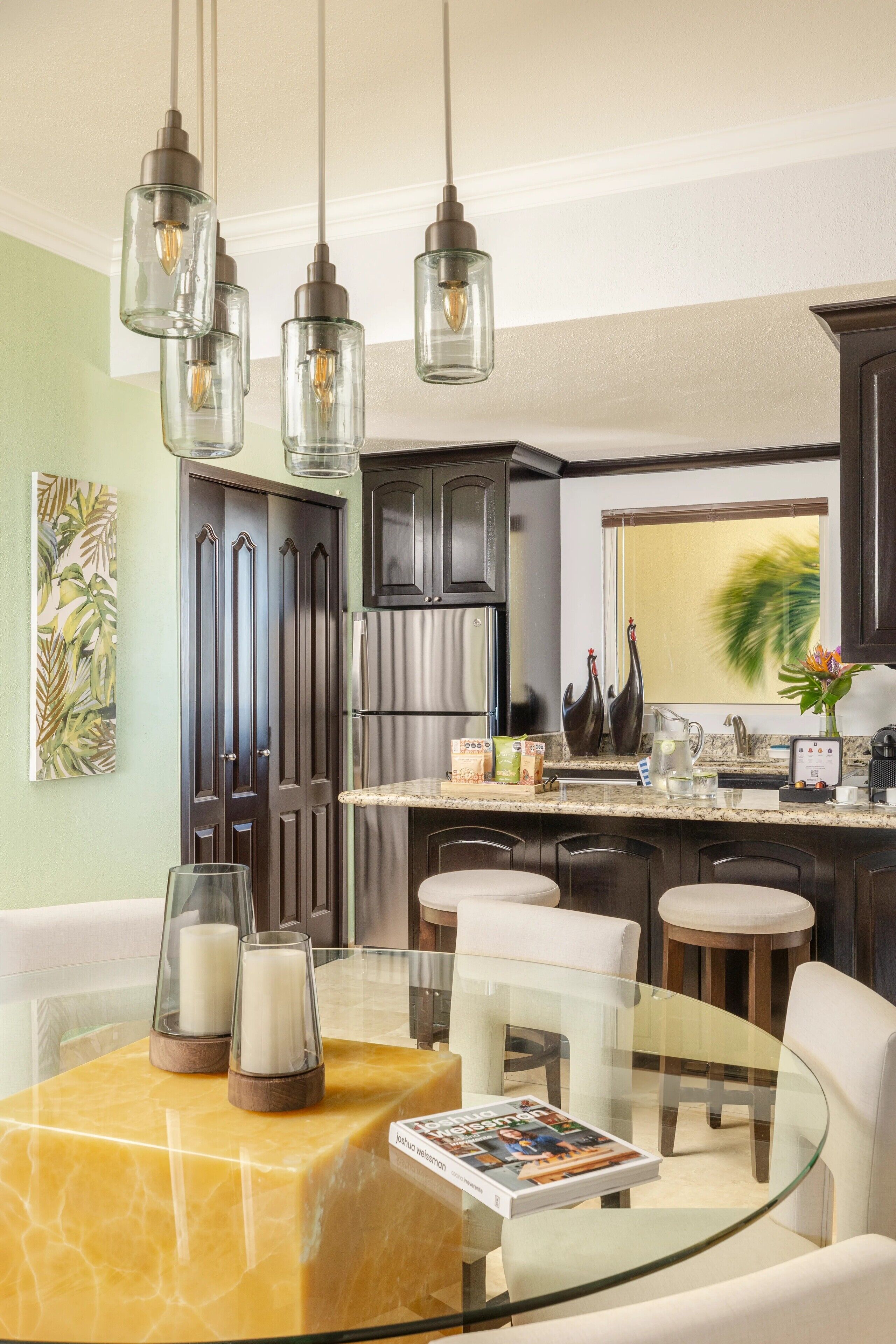 Una cocina moderna con armarios de madera oscura, un refrigerador de acero inoxidable y una mesa de comedor de vidrio con sillas blancas.
